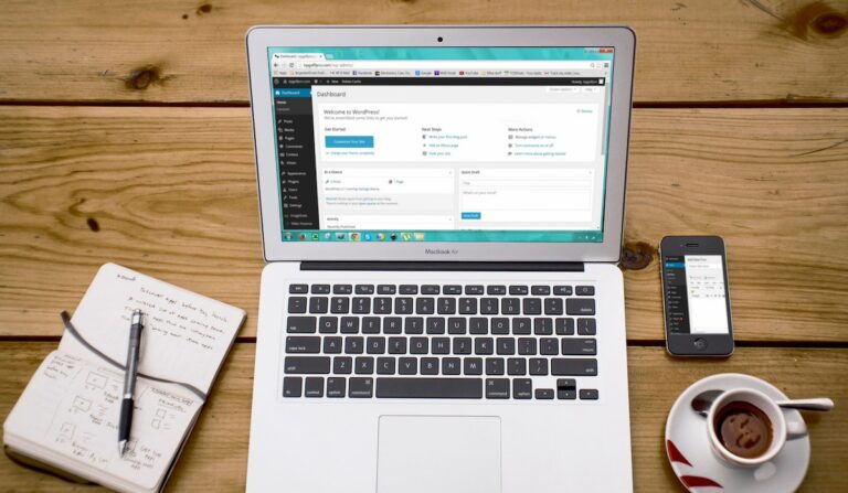 Turned-on Macbook Air Beside Black Iphone 4, Cup of Tea, and Notebook on Brown Wooden Surface