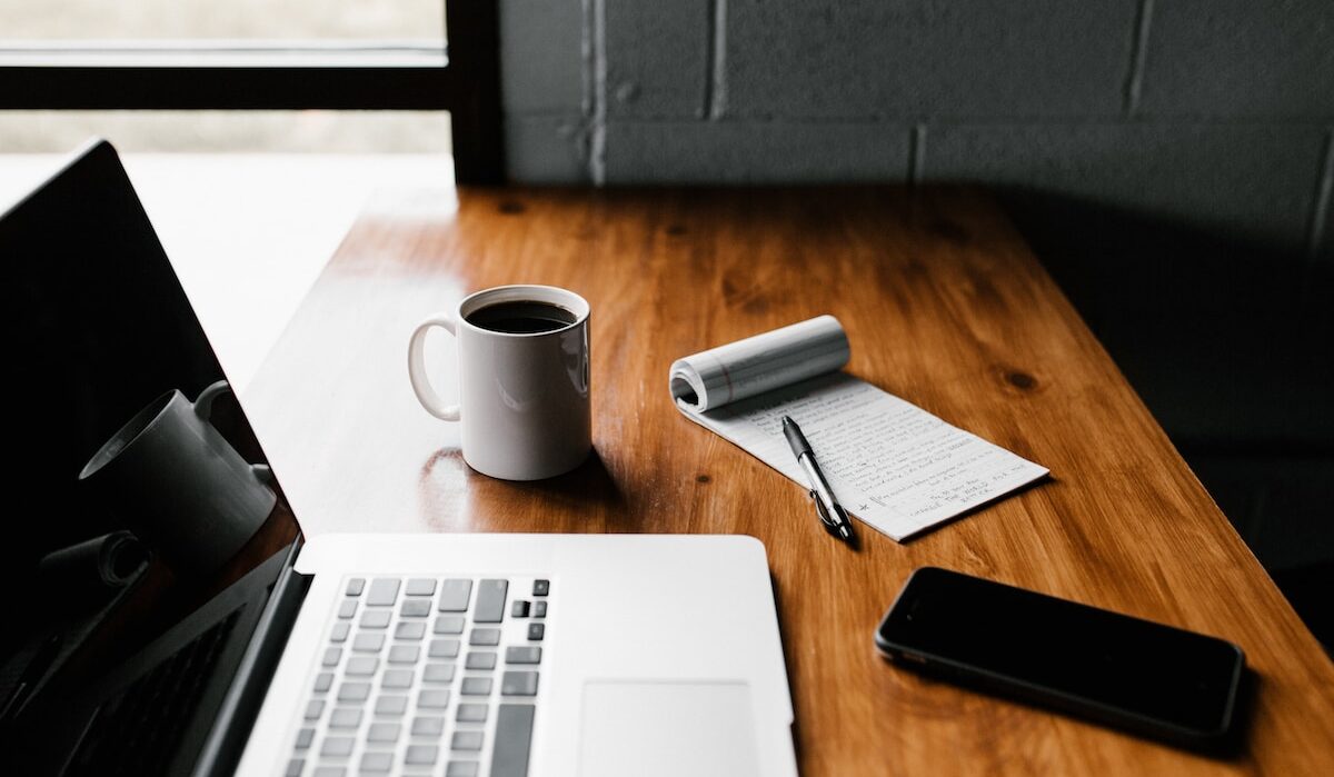 MacBook Pro, white ceramic mug,and black smartphone on table